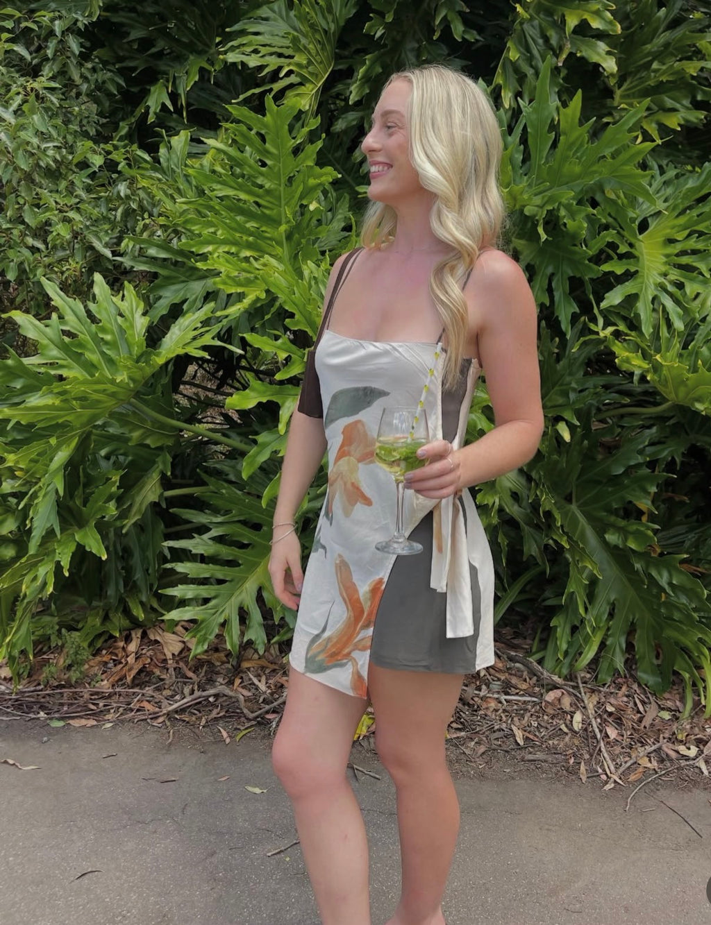 Woman holding a drink in front of green foliage