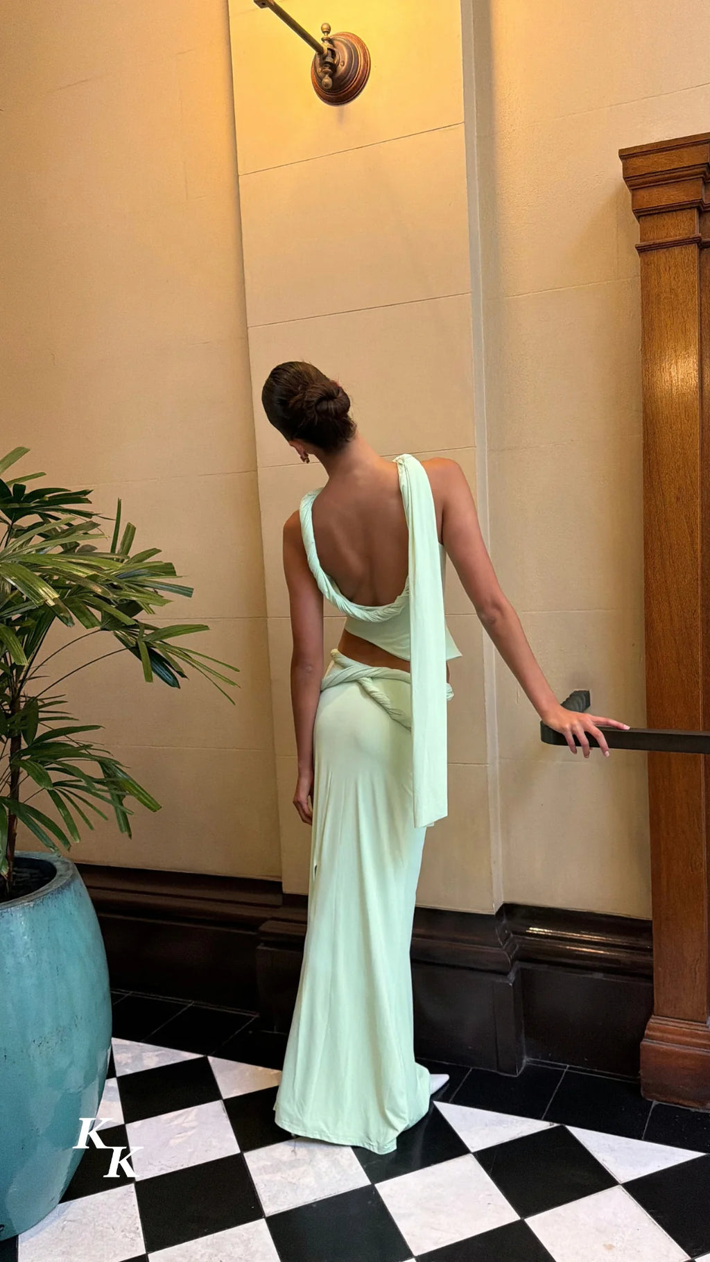 Back view of the Koster Kulture Athena Set in soft lime green, featuring an open-back top with twisted detailing, a long draped shoulder sash and a matching low-waisted maxi skirt.