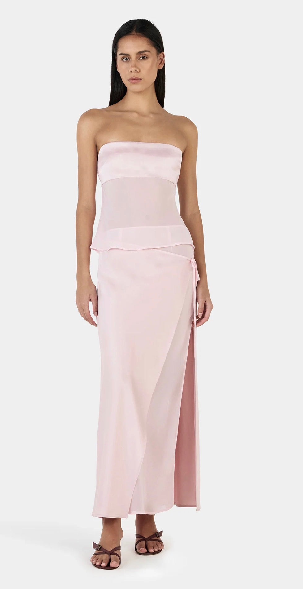 Woman wearing a strapless pink gown with a slit on a white background