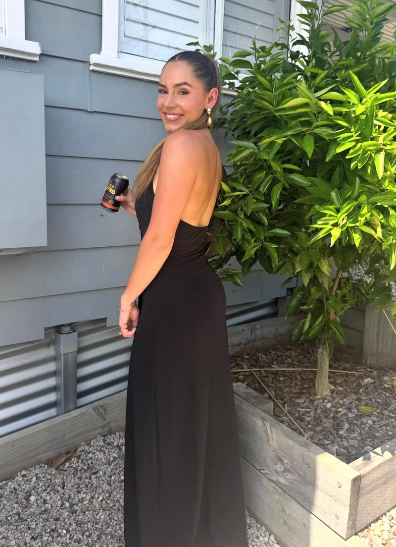 Woman in a black dress standing outside a house with plants in the background. - @breejanedawson