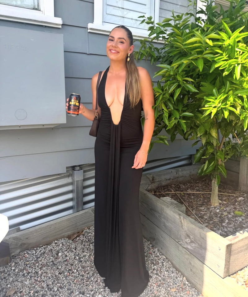 Woman in a black dress holding a can outdoors next to a house. - @breejanedawson