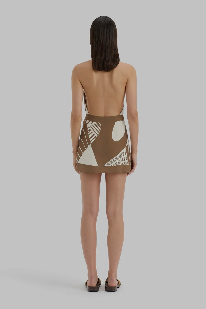 Woman wearing a brown dress with geometric cut-out design on a gray background