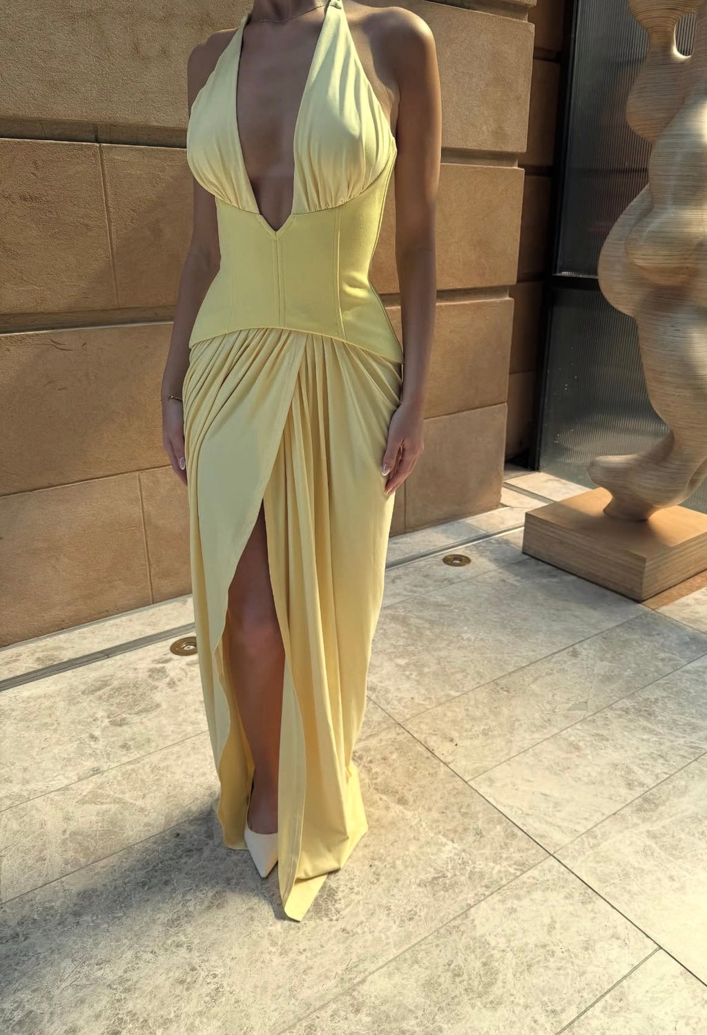 Woman wearing a yellow dress standing against a stone wall.