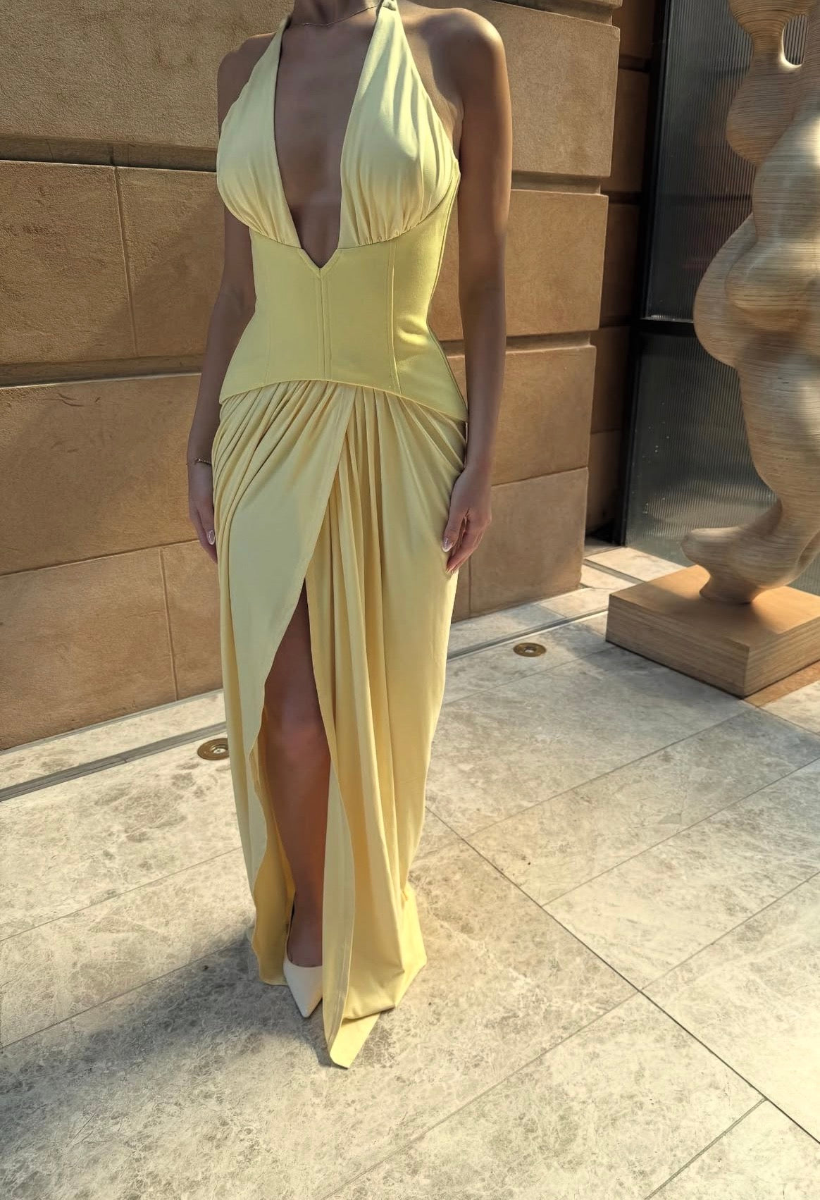 Woman wearing a yellow dress standing against a stone wall.