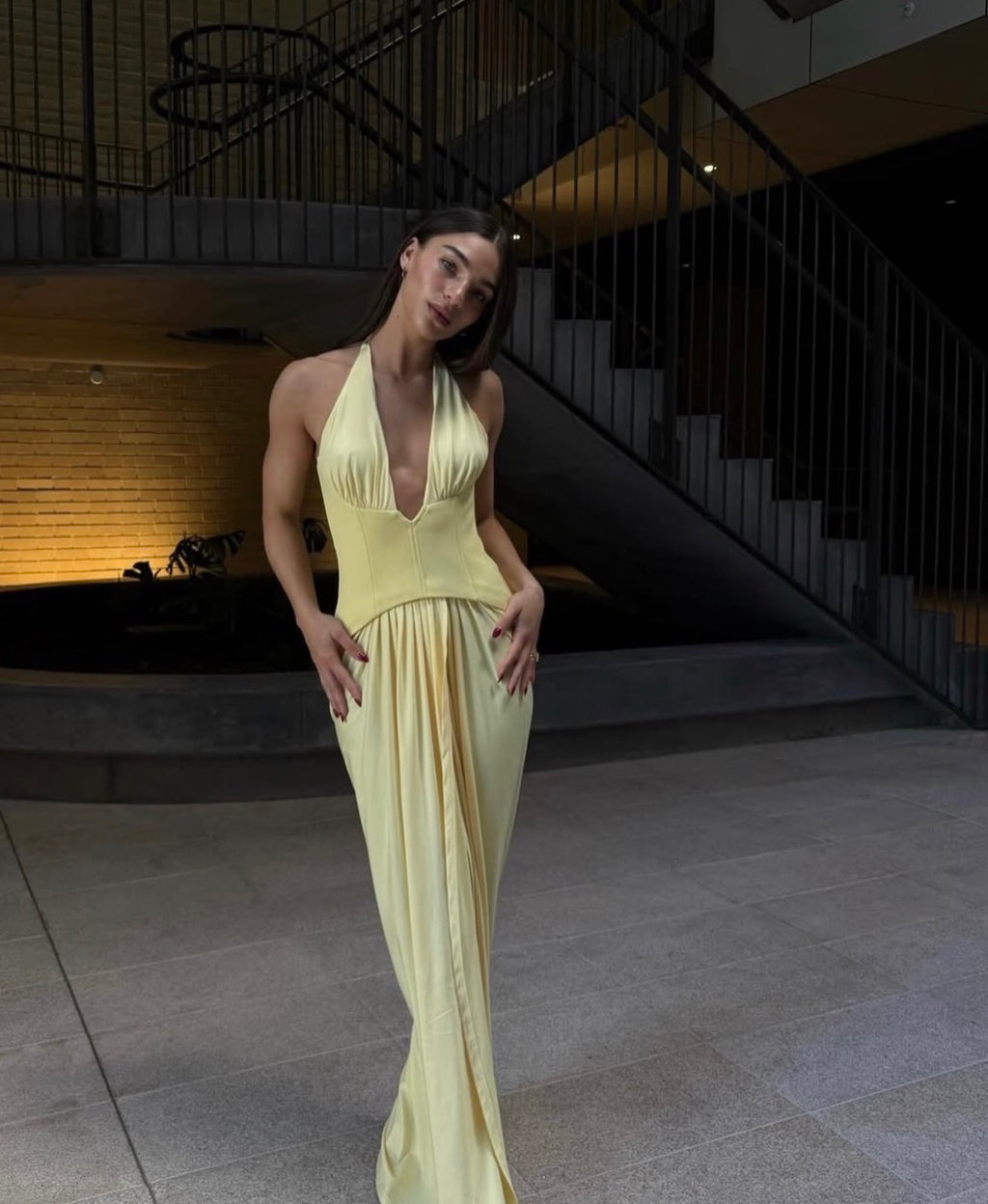 Woman in a yellow evening gown standing in a modern indoor setting with stairs.