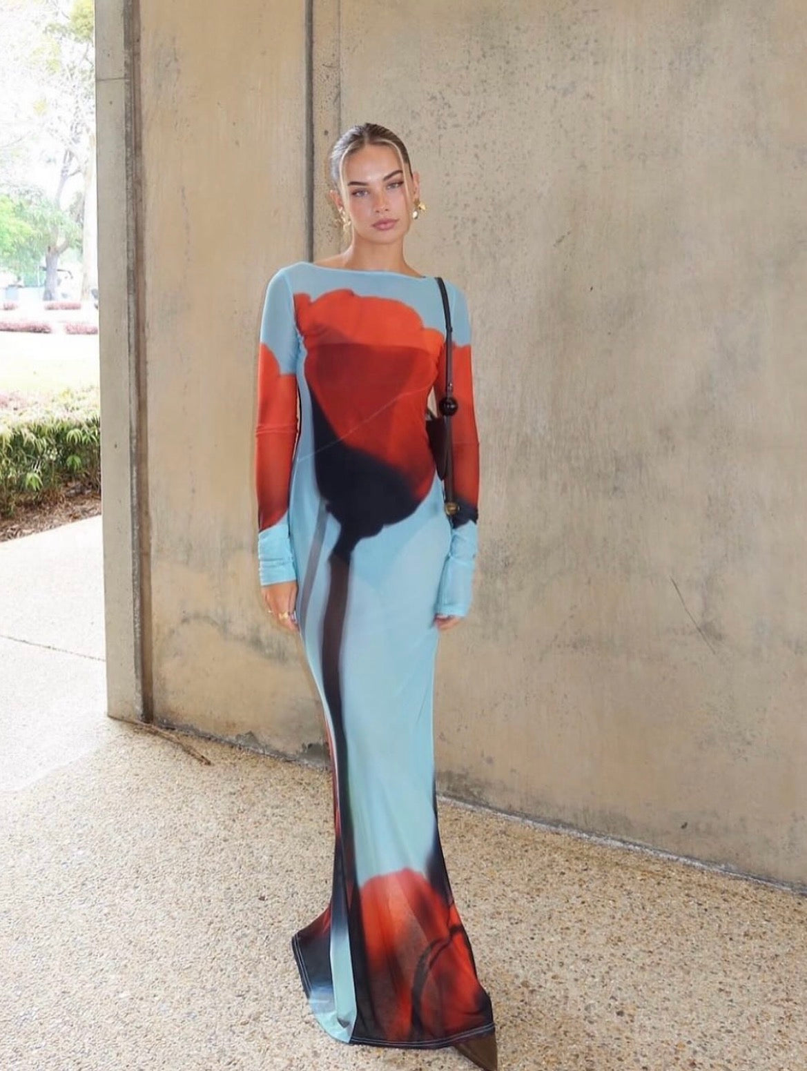 Woman wearing a long, colorful dress with abstract patterns against a plain wall.