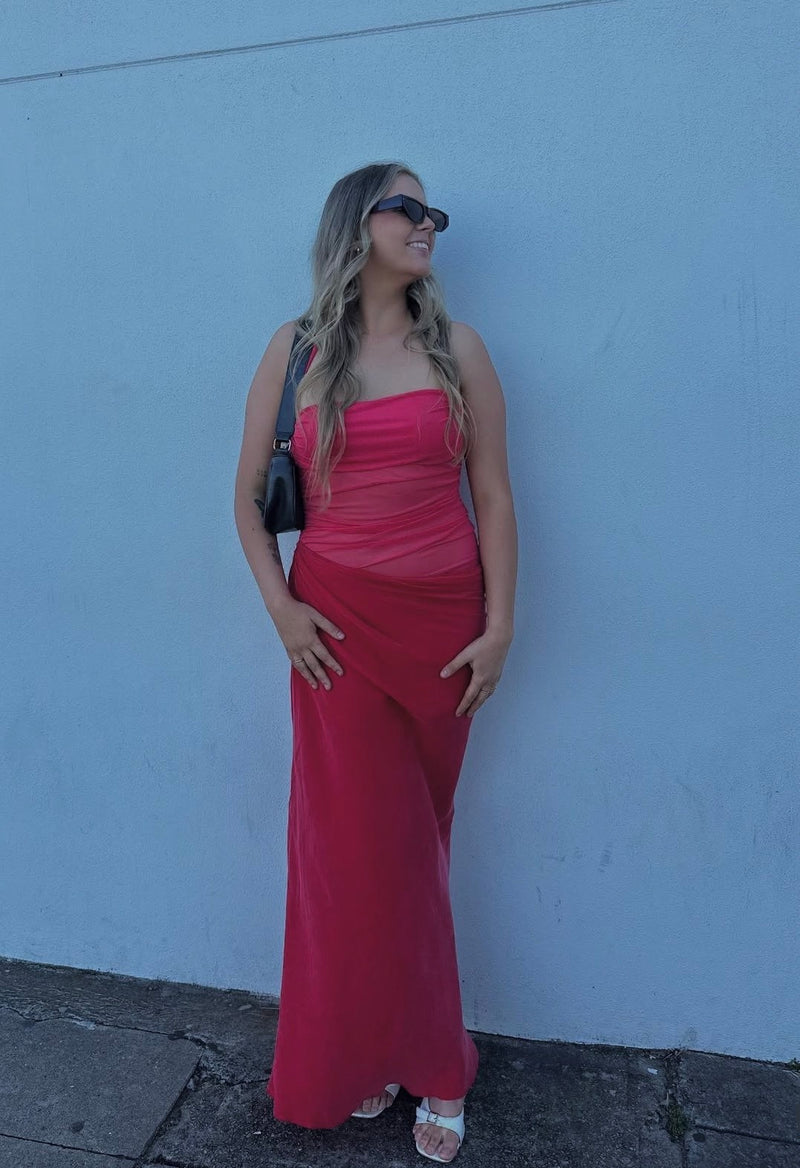 Woman in a red dress standing against a light blue wall. - @libbygouw