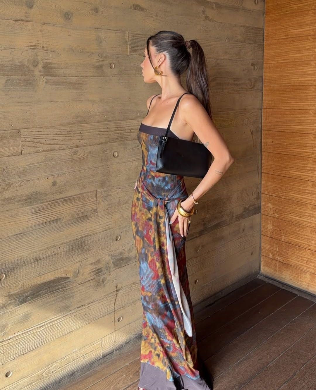 Woman in a colorful dress standing against a wooden wall. - @rahneebransby