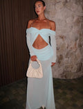 Woman in a light blue off-shoulder dress holding a beige clutch against a stone wall. - @alesha.beggs