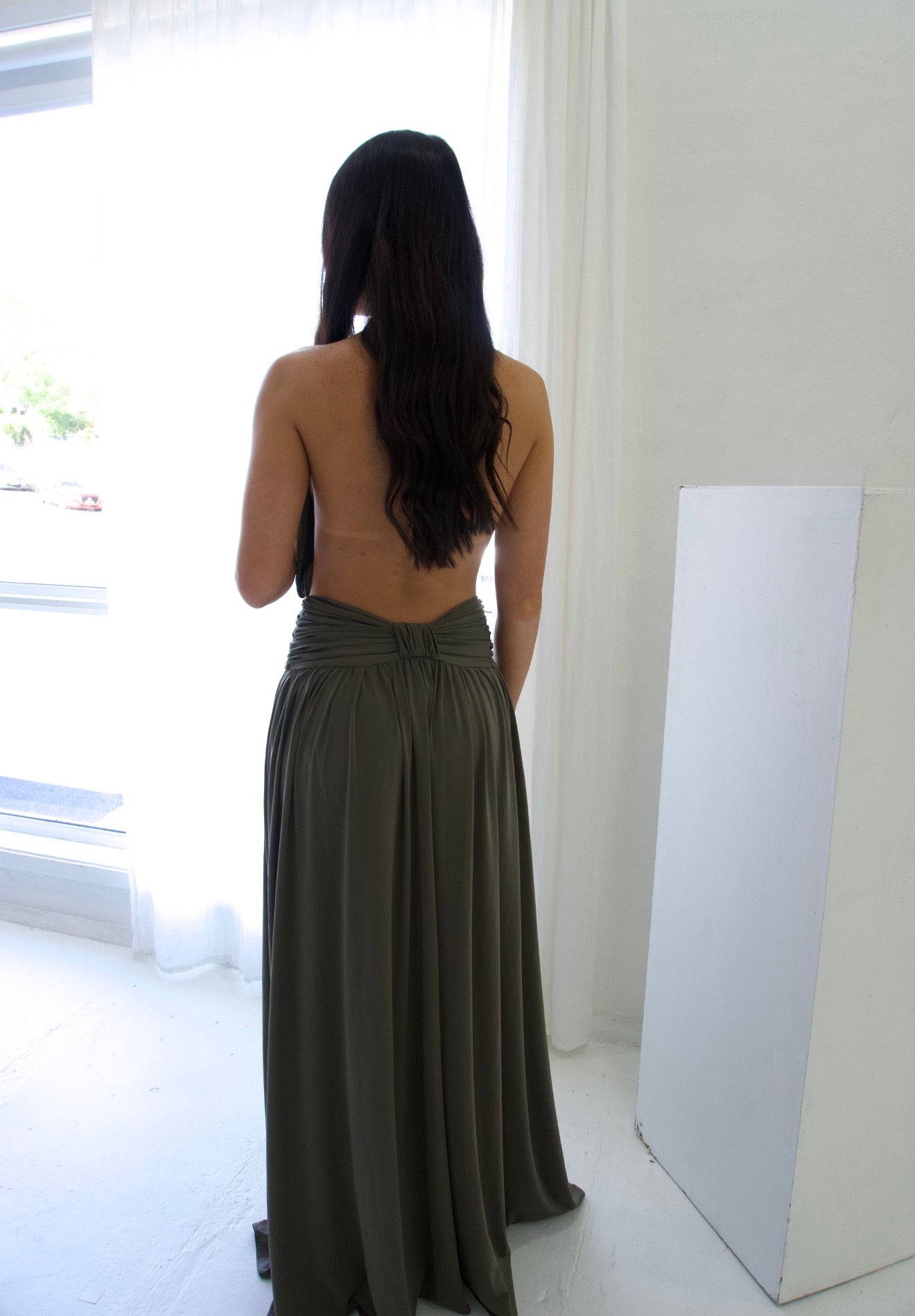 Woman wearing a long, dark green dress in a minimal white room.