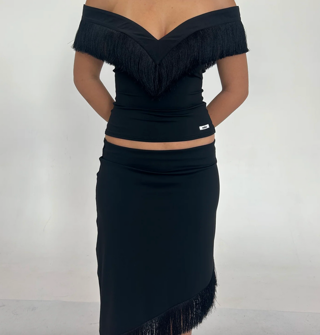 Model wearing the Nalissa Luna Set in black, featuring an off-the-shoulder V-neck top with statement fringe detailing and a matching low-rise midaxi skirt with an asymmetrical fringed hem.