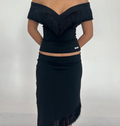 Model wearing the Nalissa Luna Set in black, featuring an off-the-shoulder V-neck top with statement fringe detailing and a matching low-rise midaxi skirt with an asymmetrical fringed hem.