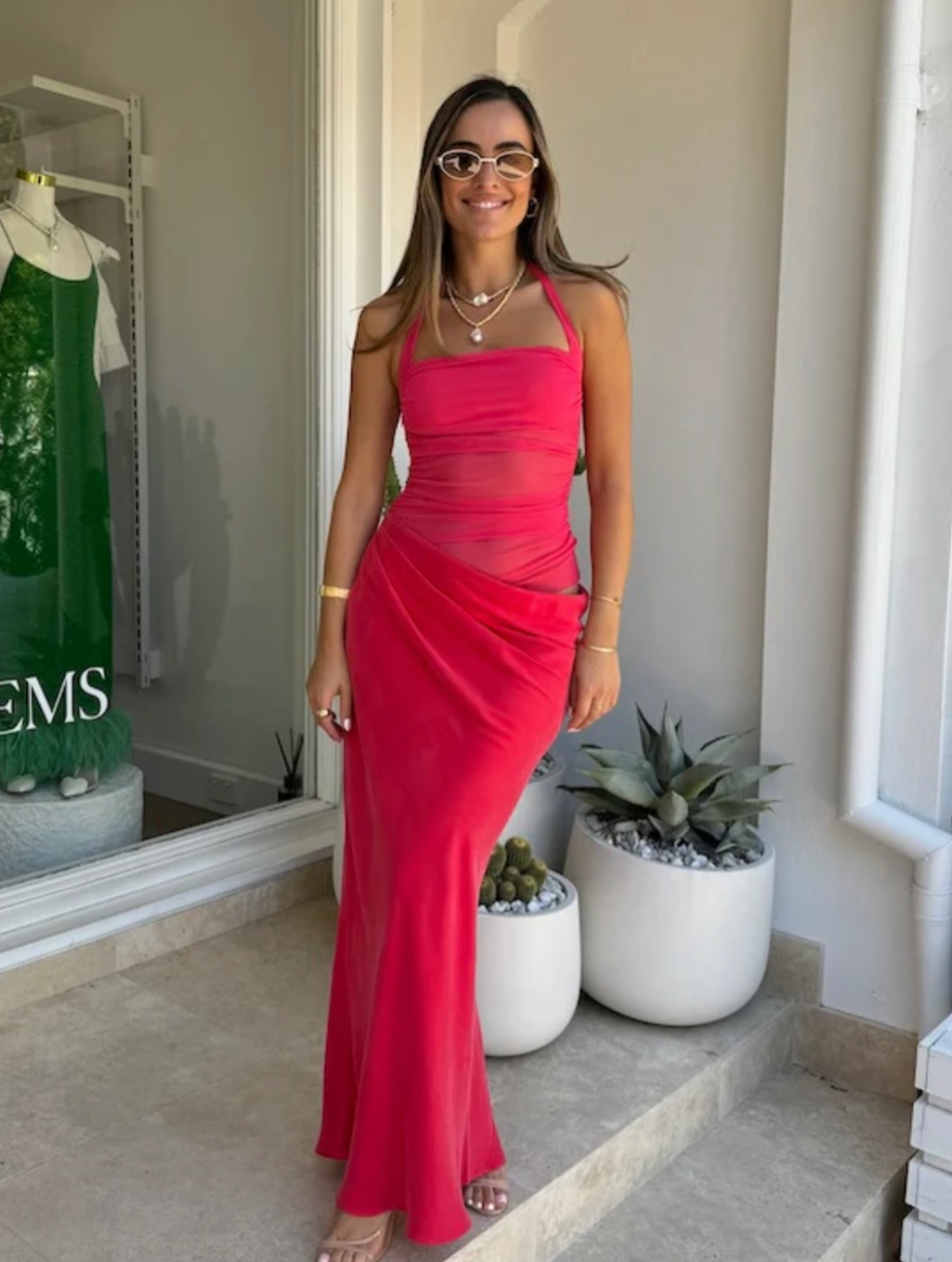 Woman in a red dress standing in a store with plants and clothing in the background