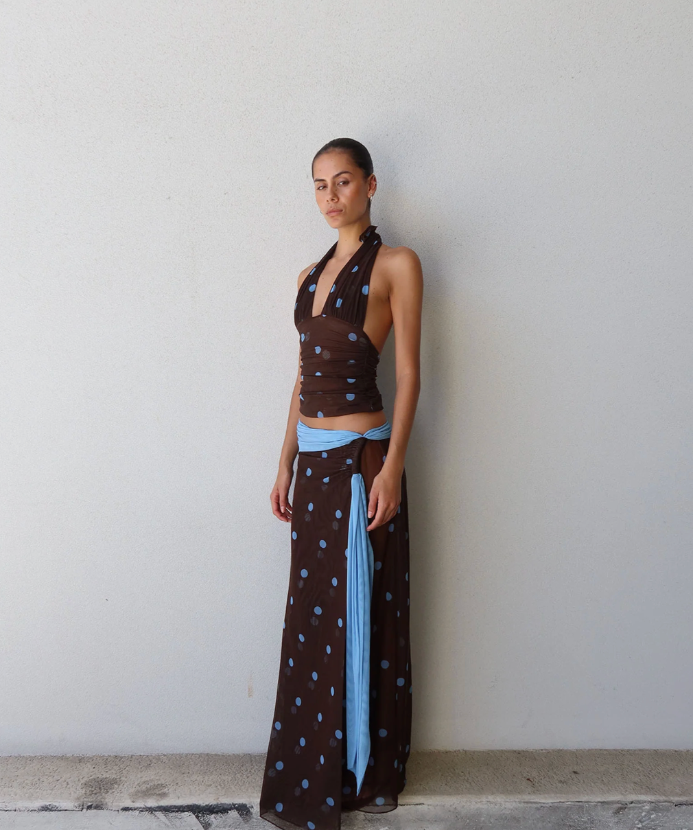 Woman wearing a brown and blue polka dot outfit against a white wall.