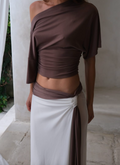 Person wearing a brown top and white skirt against a neutral background