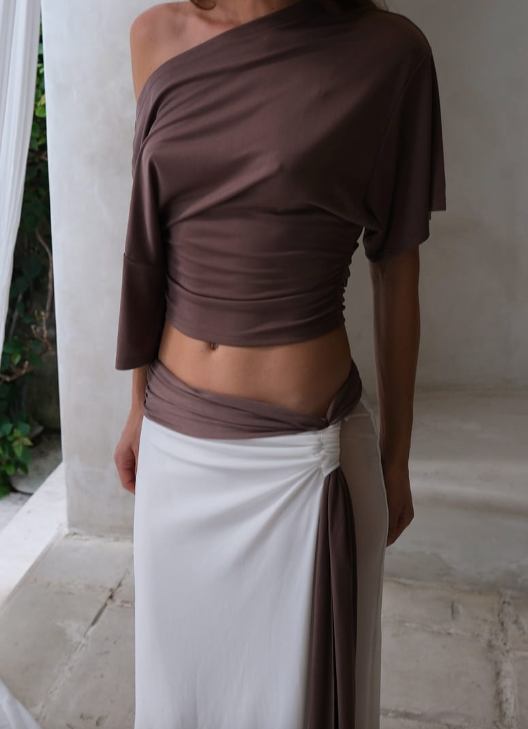 Person wearing a brown top and white skirt against a neutral background