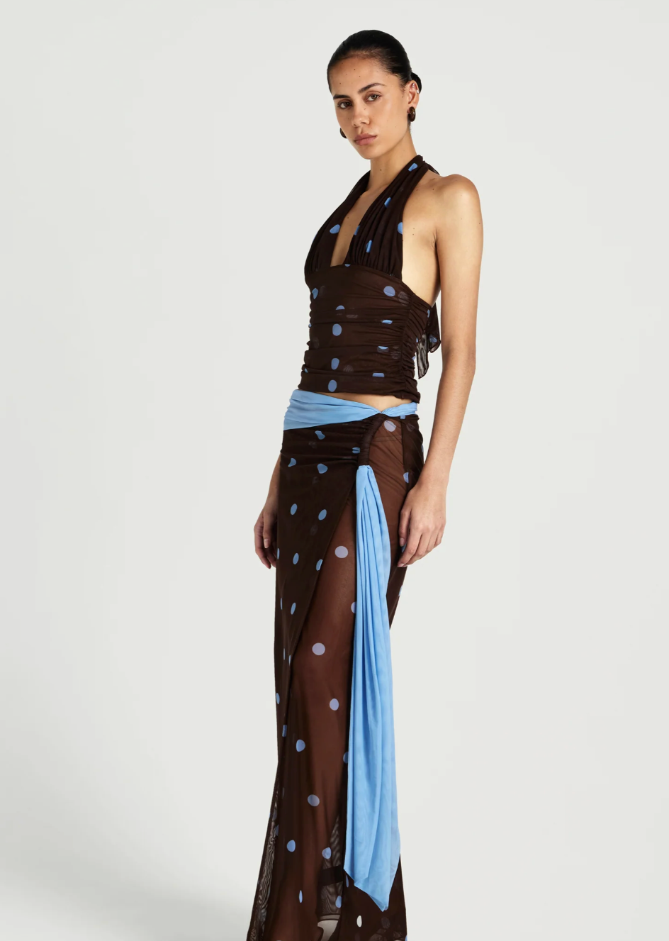 Woman wearing a brown halter top with polka dots and a sheer skirt with blue accents on a white background