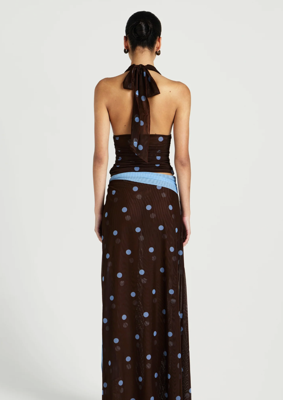 Woman wearing a brown halter neck dress with blue polka dots on a white background