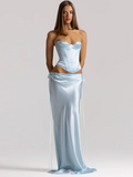 A model wearing a light blue satin two-piece set consisting of a strapless corset-style top and a matching satin wrap skirt with long side ties, photographed against a plain light gray studio background.