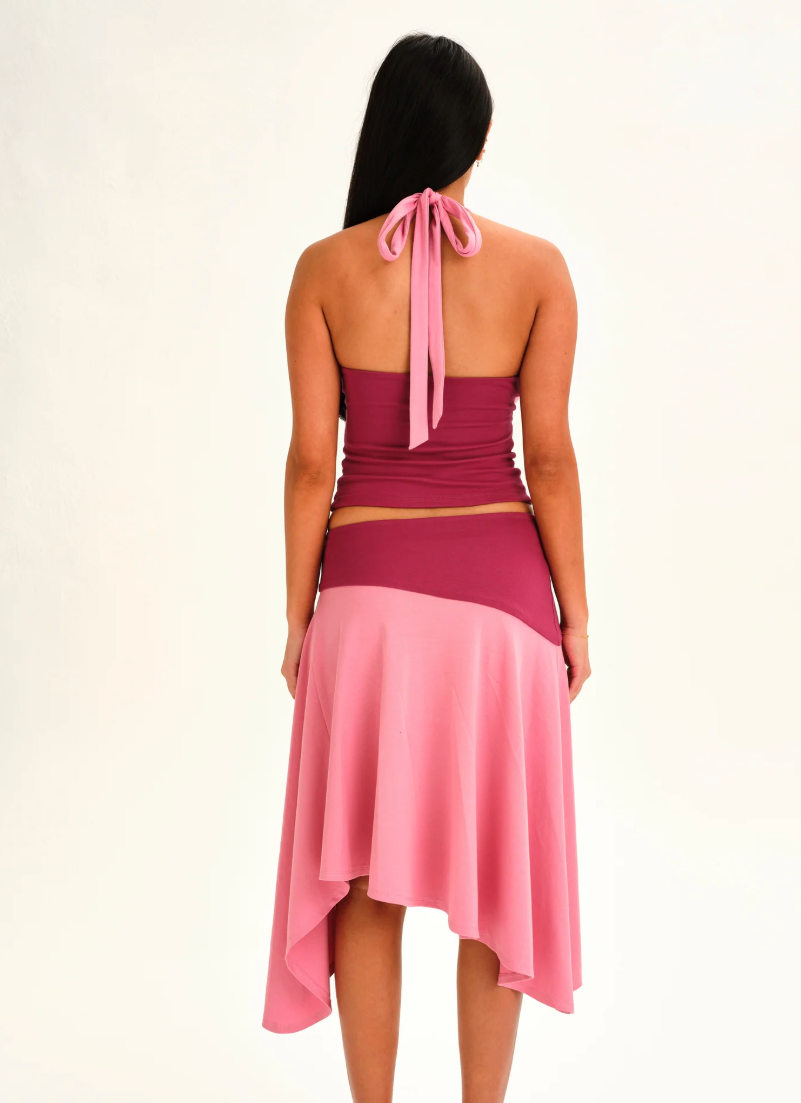 A woman shown from the back wearing a two-tone pink dress with a halter top and flared skirt, photographed against a plain light background.